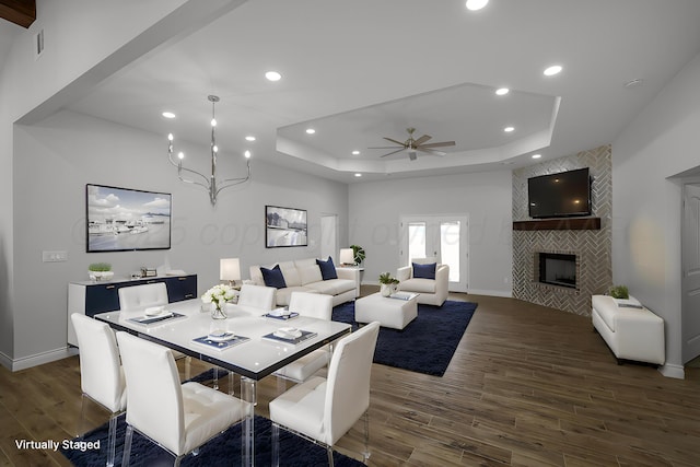 dining space featuring ceiling fan with notable chandelier, french doors, a tile fireplace, and a tray ceiling