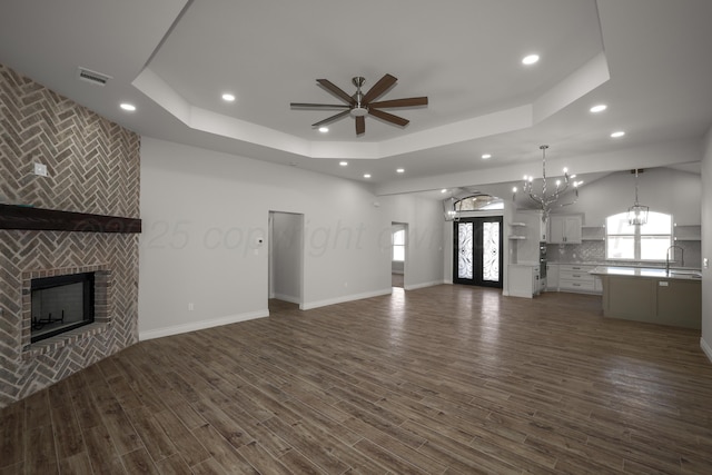 unfurnished living room featuring a tray ceiling, a fireplace, dark hardwood / wood-style floors, and ceiling fan with notable chandelier