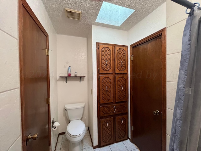 bathroom with toilet, tile patterned flooring, a textured ceiling, and a skylight