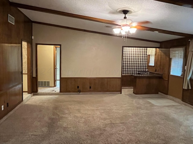 carpeted spare room with ceiling fan, wooden walls, vaulted ceiling with beams, and a textured ceiling