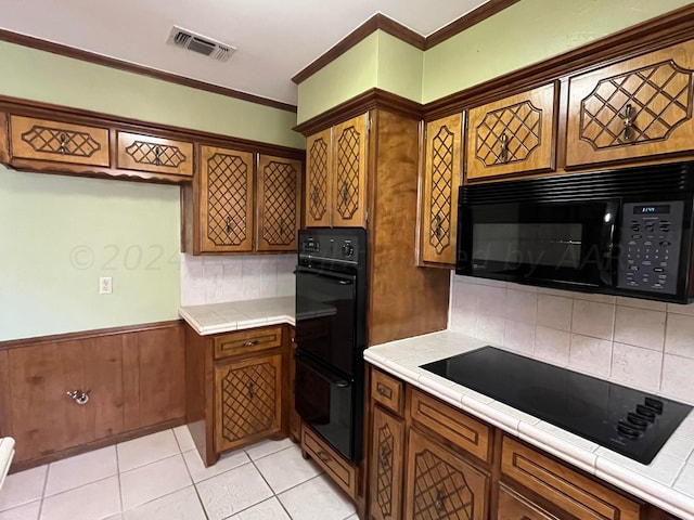 kitchen with tile countertops, black appliances, light tile patterned floors, crown molding, and backsplash