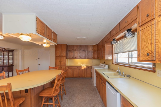 kitchen with dishwasher, sink, washer / clothes dryer, light colored carpet, and a breakfast bar area