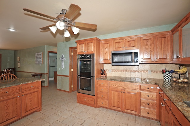1206 Olive St, Stratford, TX 79084 - kitchen featuring appliances with stainless steel finishes, decorative backsplash, ceiling fan, and brown cabinetry