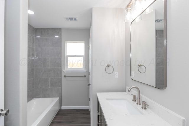 bathroom with wood-type flooring, vanity, and tiled shower / bath