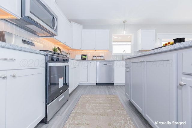 kitchen featuring white cabinetry, light wood-type flooring, appliances with stainless steel finishes, and decorative light fixtures