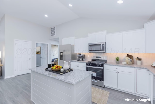 kitchen with light hardwood / wood-style flooring, tasteful backsplash, a kitchen island, white cabinetry, and appliances with stainless steel finishes