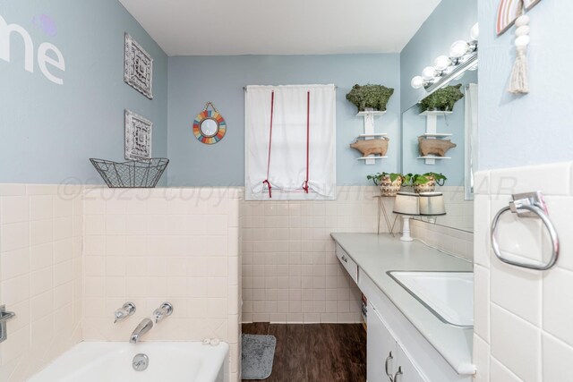107 Elm St, Hereford, TX 79045 - bathroom with a wainscoted wall, wood finished floors, vanity, tile walls, and a garden tub