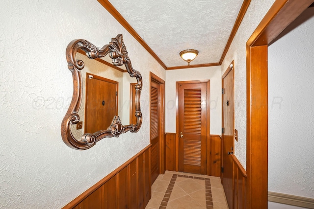 hallway featuring wooden walls, wainscoting, a textured ceiling, light tile patterned floors, and ornamental molding