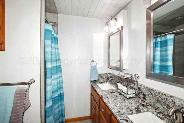 bathroom featuring a shower with shower curtain, double vanity, baseboards, and a sink