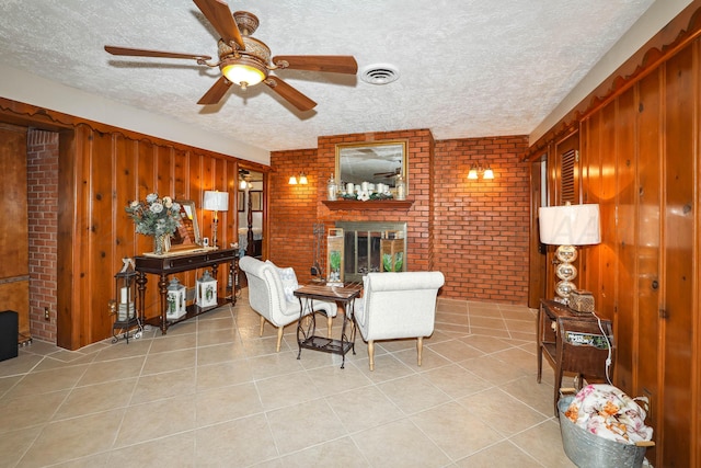 living area featuring a textured ceiling, a brick fireplace, light tile patterned floors, and brick wall