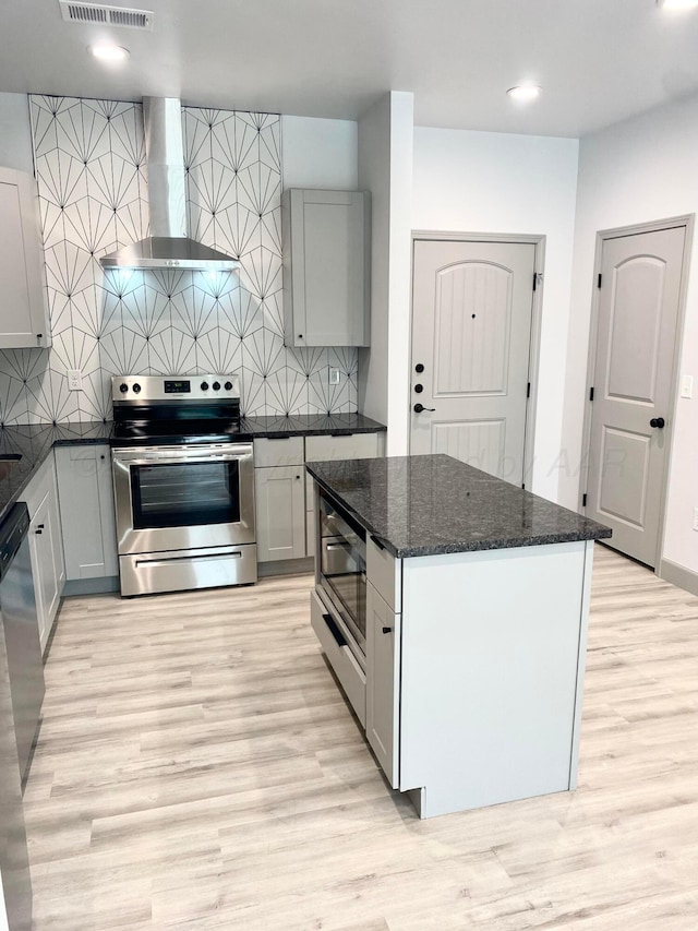 2 S Hunsley Hills Blvd, Canyon, TX 79015 - kitchen featuring wall chimney exhaust hood, stainless steel appliances, light wood finished floors, dark stone countertops, and tasteful backsplash