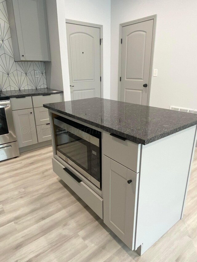 2 S Hunsley Hills Blvd, Canyon, TX 79015 - kitchen with light wood-type flooring, appliances with stainless steel finishes, tasteful backsplash, dark stone countertops, and a center island