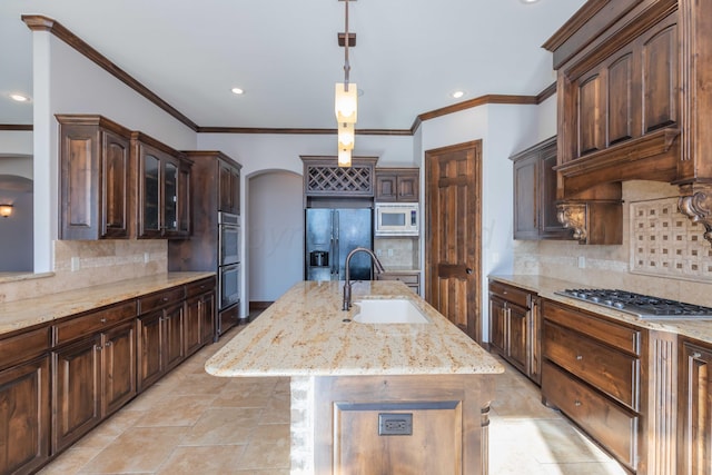 kitchen with a kitchen island with sink, sink, light stone countertops, appliances with stainless steel finishes, and decorative light fixtures