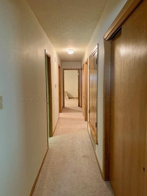 corridor with a textured ceiling and light carpet