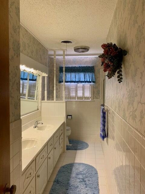 bathroom with toilet, tile patterned floors, tile walls, a textured ceiling, and vanity