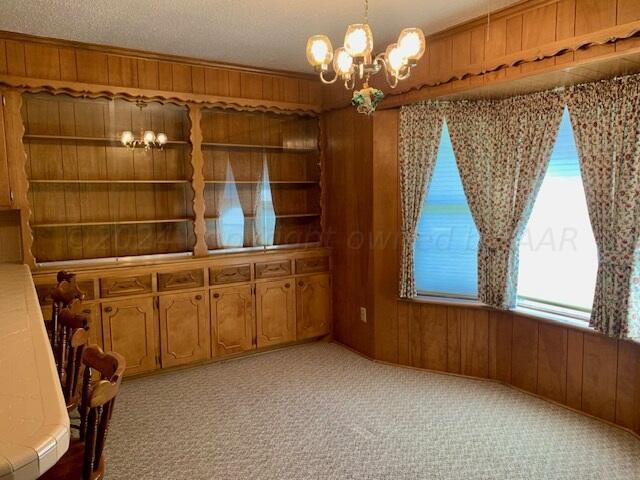 unfurnished dining area with a textured ceiling, light carpet, wooden walls, and an inviting chandelier