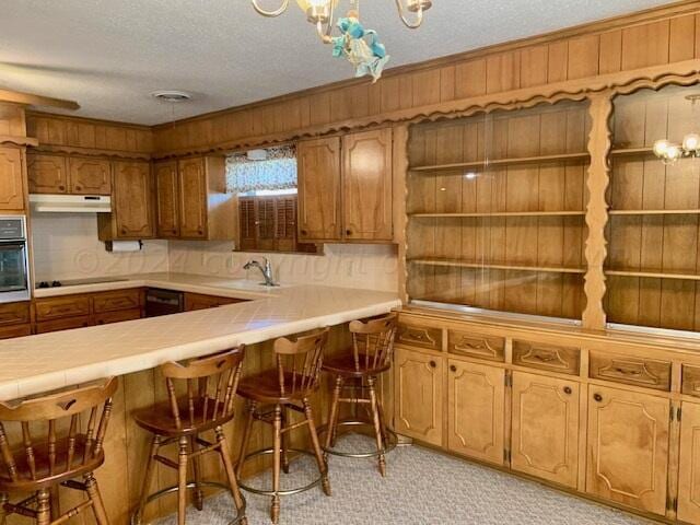 kitchen featuring tile countertops, sink, a breakfast bar area, a textured ceiling, and stainless steel oven