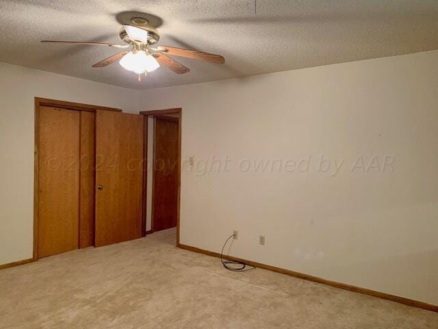 unfurnished bedroom featuring a closet, a textured ceiling, light colored carpet, and ceiling fan