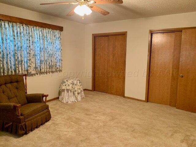 living area featuring a textured ceiling, light colored carpet, and ceiling fan