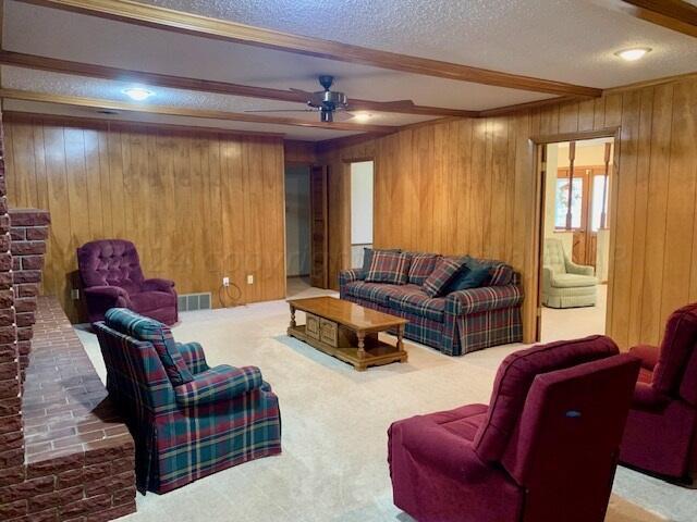 living room featuring a textured ceiling, wooden walls, and beam ceiling