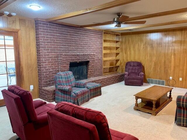 living room featuring carpet, a textured ceiling, wood walls, a brick fireplace, and ceiling fan