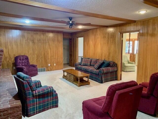 carpeted living room featuring wooden walls, a textured ceiling, ceiling fan, and beam ceiling