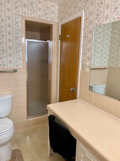 bathroom featuring toilet, vanity, tile walls, and a shower with door