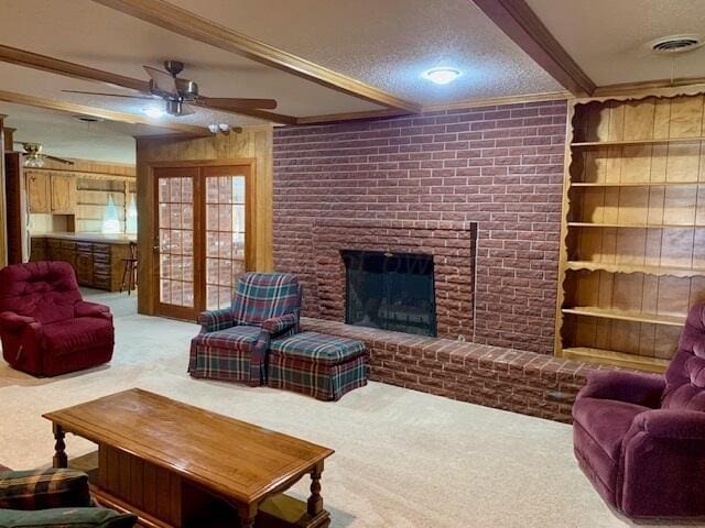 carpeted living room with a brick fireplace, a textured ceiling, beamed ceiling, ceiling fan, and crown molding