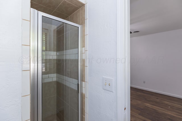 bathroom featuring wood finished floors, a shower stall, a textured wall, and baseboards