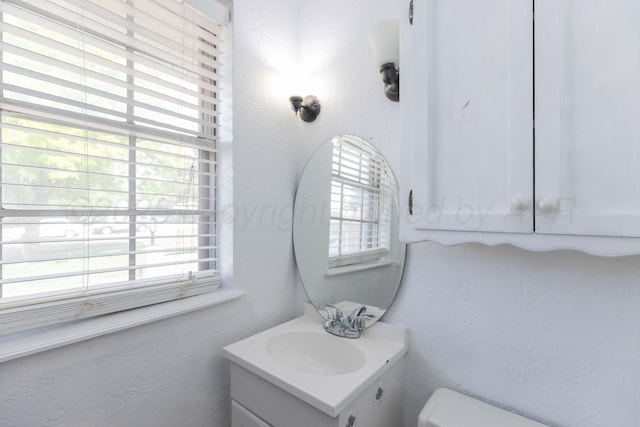 half bathroom featuring a textured wall, vanity, and toilet