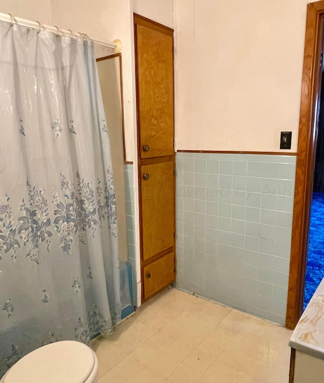 bathroom with a shower with curtain, toilet, and tile walls