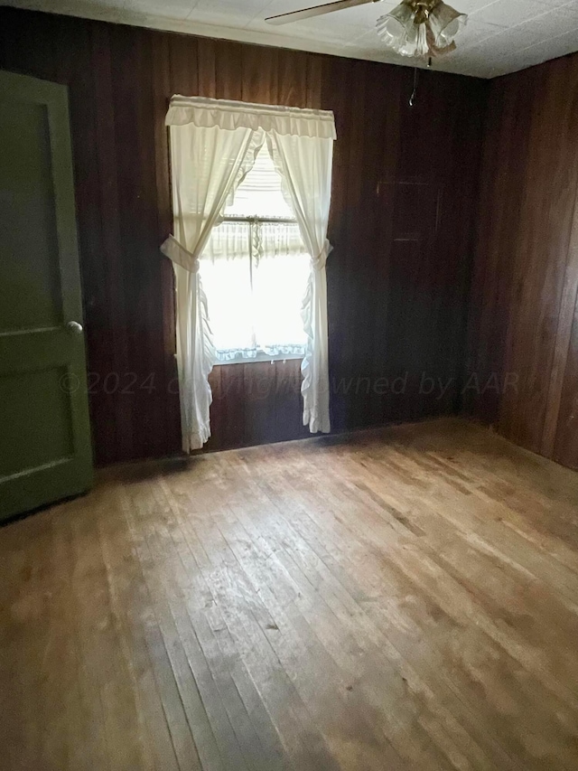 spare room featuring hardwood / wood-style floors, ceiling fan, and wood walls