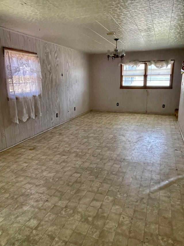 spare room featuring a healthy amount of sunlight, wooden walls, and a notable chandelier