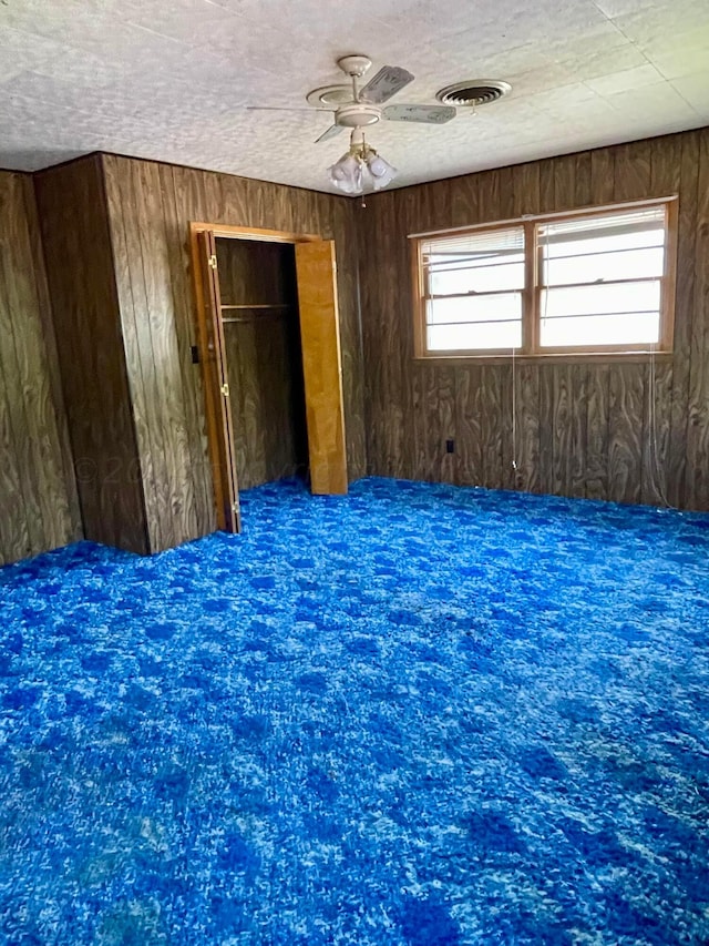 spare room featuring ceiling fan, wood walls, and a textured ceiling