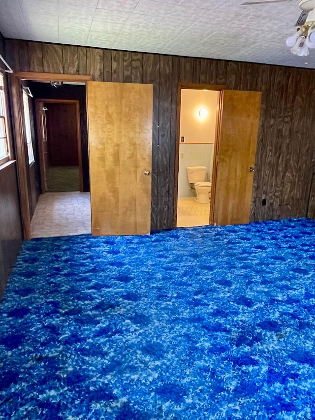 unfurnished bedroom with wooden walls, ceiling fan, and connected bathroom