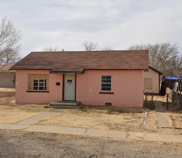 ranch-style home featuring concrete block siding, roof with shingles, and fence