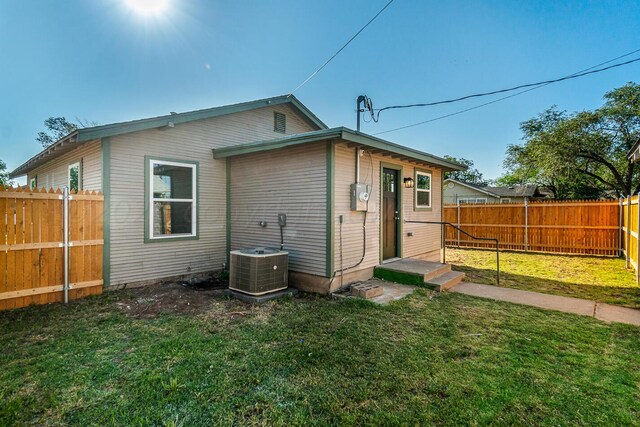 rear view of property with central air condition unit and a lawn