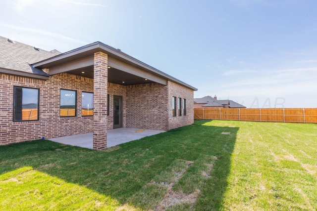 rear view of house featuring fence, a lawn, brick siding, and a patio