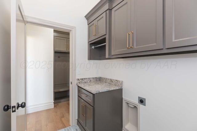 laundry room featuring light wood finished floors, hookup for an electric dryer, and cabinet space
