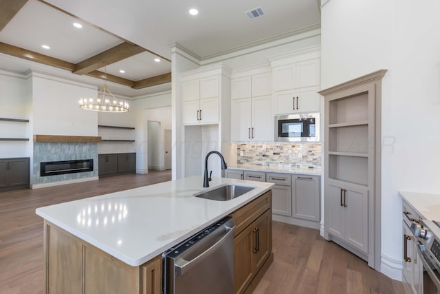 kitchen with wood finished floors, a sink, decorative backsplash, an inviting chandelier, and appliances with stainless steel finishes