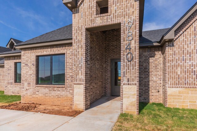doorway to property with brick siding and a shingled roof