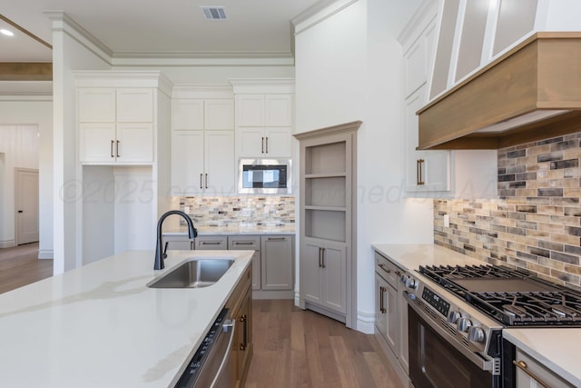 kitchen featuring a sink, wood finished floors, custom range hood, light countertops, and appliances with stainless steel finishes