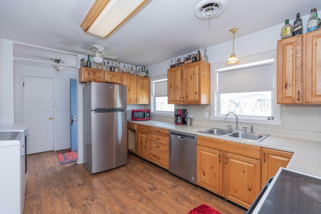 kitchen with pendant lighting, dark wood finished floors, light countertops, appliances with stainless steel finishes, and a sink