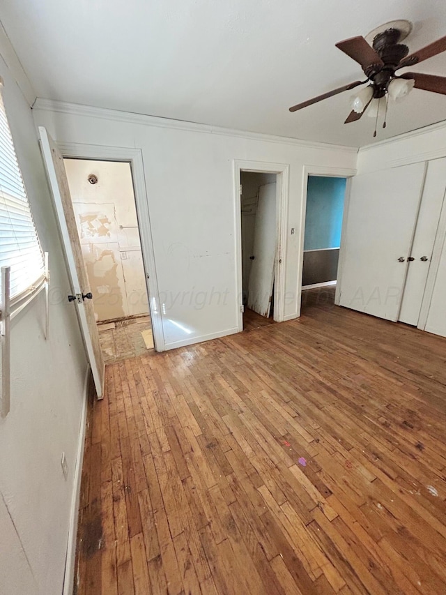 unfurnished bedroom with ensuite bathroom, hardwood / wood-style flooring, ornamental molding, ceiling fan, and multiple closets