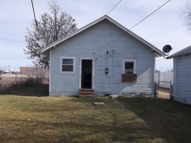 rear view of house with entry steps, a lawn, and fence