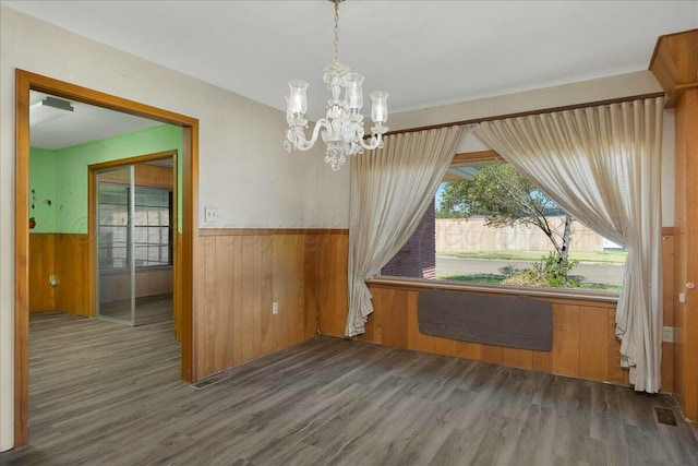 unfurnished dining area featuring dark hardwood / wood-style flooring, wooden walls, and an inviting chandelier