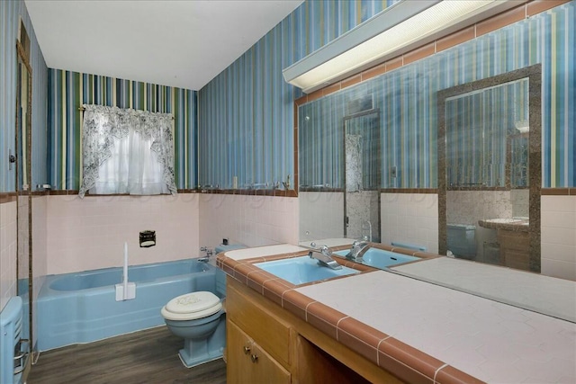 bathroom featuring vanity, hardwood / wood-style flooring, toilet, tile walls, and a tub