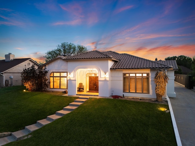 mediterranean / spanish home featuring fence, concrete driveway, a tile roof, a front yard, and stucco siding