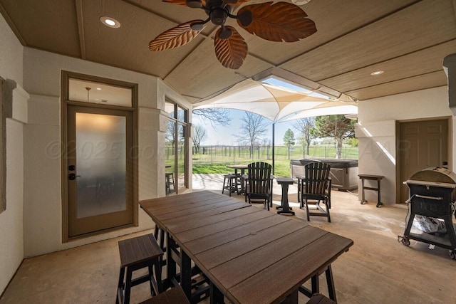 view of patio / terrace featuring outdoor dining space, ceiling fan, glass enclosure, and a hot tub