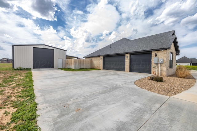 view of property exterior featuring fence, a shingled roof, concrete driveway, an outbuilding, and brick siding
